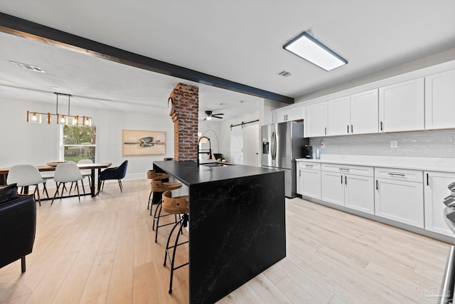 kitchen featuring beam ceiling, light wood finished floors, visible vents, backsplash, and stainless steel fridge