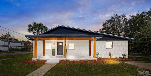 view of front of house featuring covered porch, a lawn, and brick siding