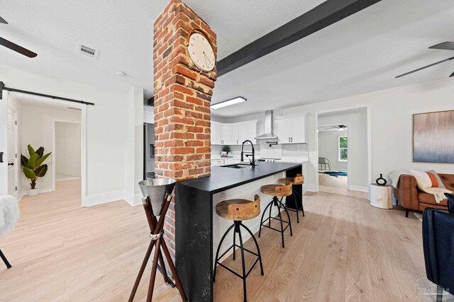 kitchen with ceiling fan, a barn door, a sink, visible vents, and wall chimney range hood