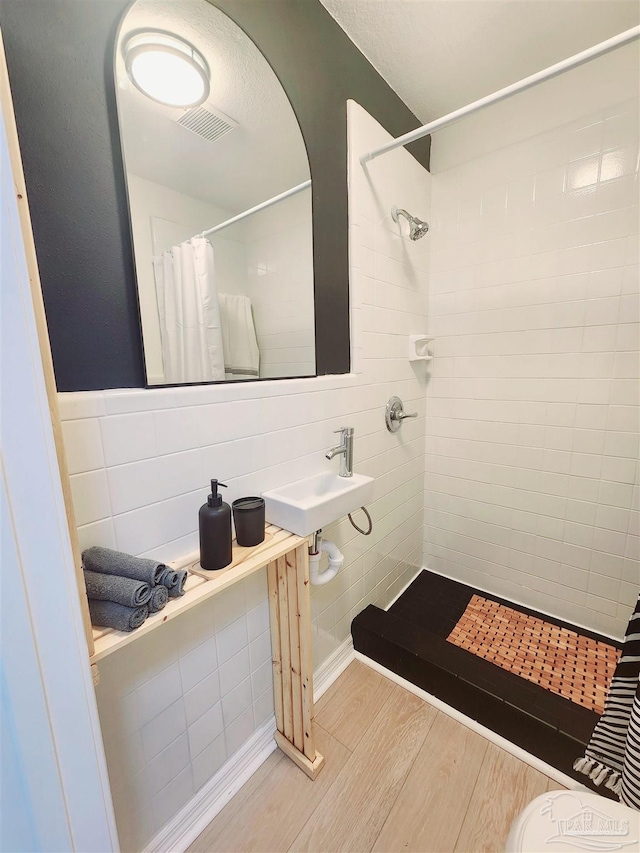 full bathroom with wood finished floors, a sink, visible vents, tile walls, and tiled shower