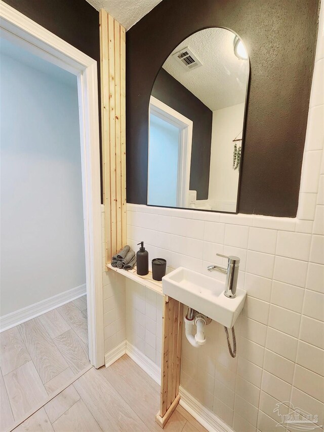 bathroom featuring a textured ceiling, visible vents, and tile walls