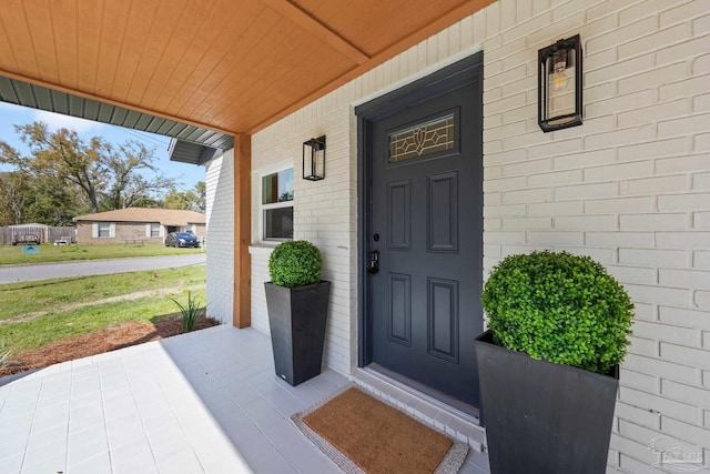 property entrance featuring covered porch, a lawn, and brick siding