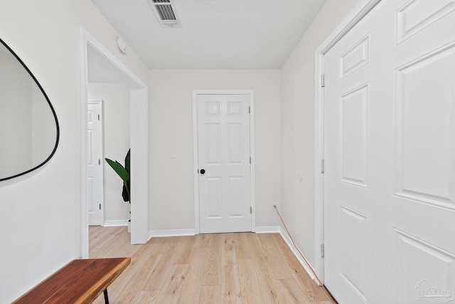 hallway with light wood-type flooring, visible vents, and baseboards