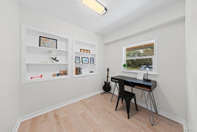 home office featuring built in shelves, light wood-type flooring, and baseboards