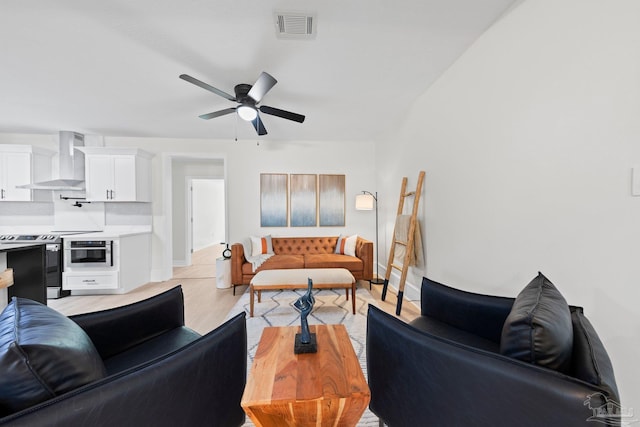 living area featuring a ceiling fan, light wood-type flooring, visible vents, and baseboards