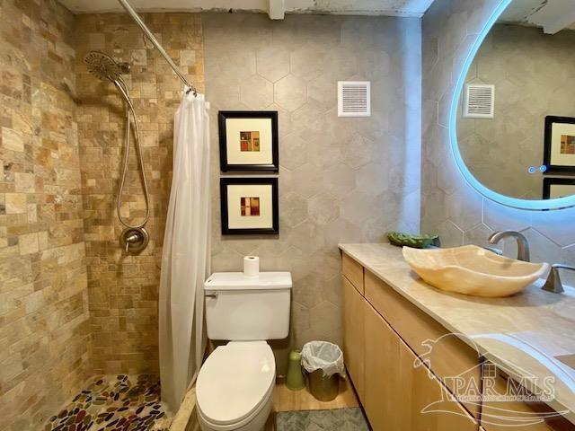 bathroom with vanity, toilet, tiled shower, and visible vents