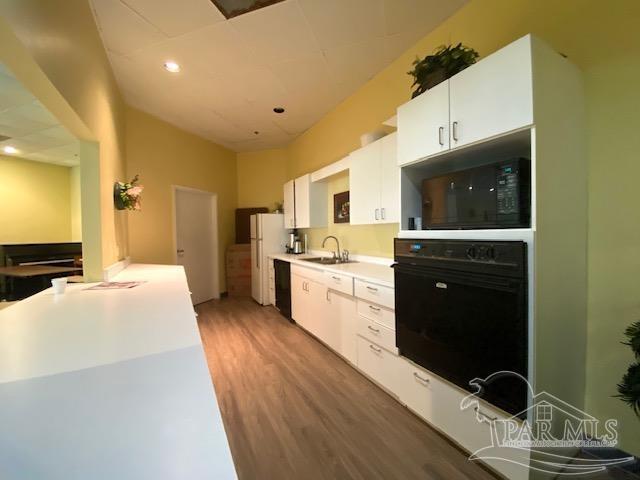 kitchen with a sink, light wood-style floors, light countertops, white cabinetry, and black appliances