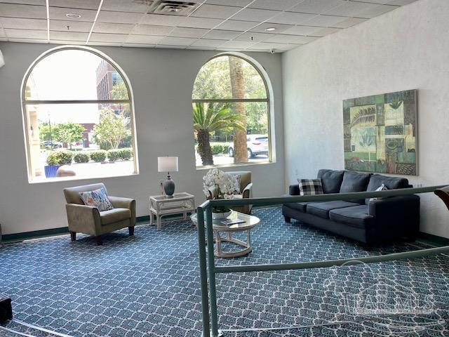 living area featuring carpet floors, baseboards, a drop ceiling, and visible vents