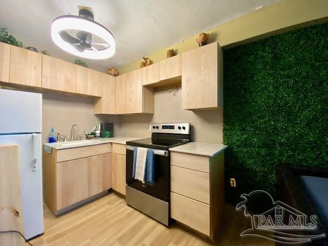 kitchen with freestanding refrigerator, a sink, light brown cabinets, and stainless steel electric range oven