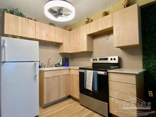 kitchen with a sink, light countertops, freestanding refrigerator, stainless steel electric stove, and light brown cabinets