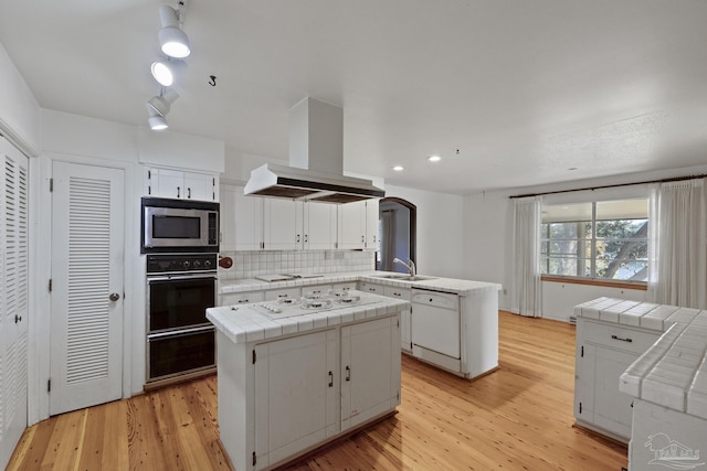 kitchen with white appliances, island range hood, tile countertops, white cabinetry, and a kitchen island