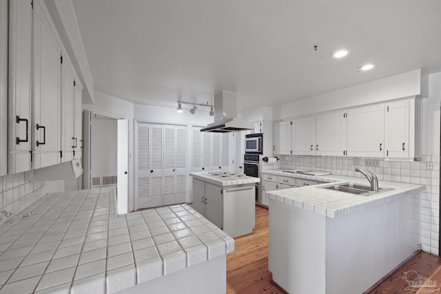 kitchen featuring sink, built in microwave, tile counters, island range hood, and kitchen peninsula