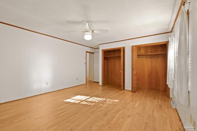 unfurnished bedroom featuring light wood-type flooring, ornamental molding, a textured ceiling, two closets, and ceiling fan