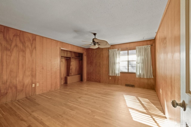 empty room with wood walls, ceiling fan, a textured ceiling, and light wood-type flooring