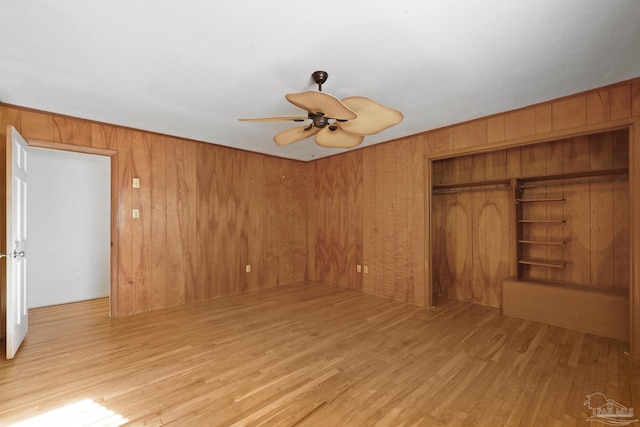 unfurnished bedroom with ceiling fan, a closet, wood walls, and light wood-type flooring