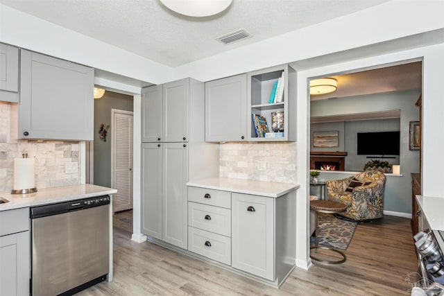 kitchen featuring light wood-type flooring, gray cabinets, stainless steel dishwasher, and tasteful backsplash