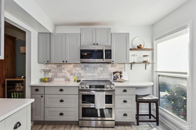 kitchen with decorative backsplash, stainless steel appliances, beverage cooler, and gray cabinetry