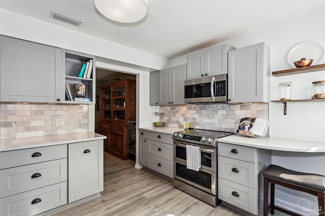 kitchen featuring gray cabinetry, stainless steel appliances, backsplash, light hardwood / wood-style floors, and a textured ceiling