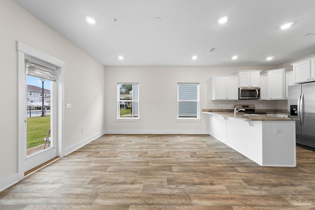 kitchen featuring dark stone countertops, appliances with stainless steel finishes, a kitchen bar, and plenty of natural light