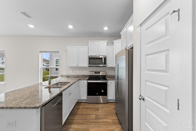 kitchen featuring stainless steel appliances, stone countertops, sink, white cabinets, and dark wood-type flooring