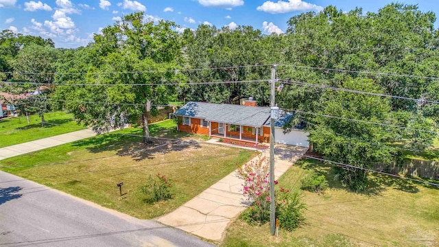 ranch-style home with brick siding, a chimney, concrete driveway, covered porch, and a front yard