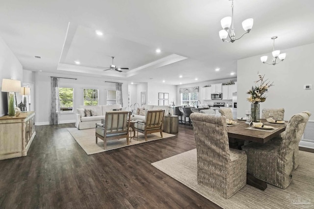 dining space with ornamental molding, ceiling fan with notable chandelier, a tray ceiling, and dark wood-type flooring