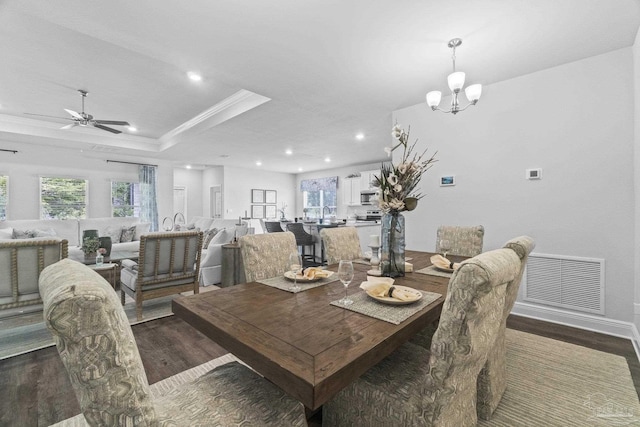 dining area featuring ceiling fan with notable chandelier, ornamental molding, dark wood-type flooring, and a tray ceiling