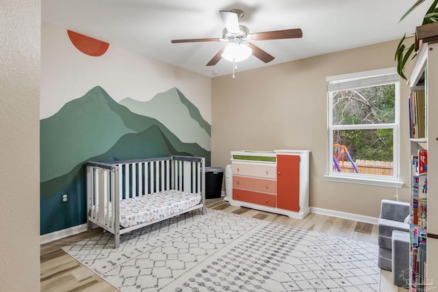 bedroom featuring ceiling fan, hardwood / wood-style floors, and a crib