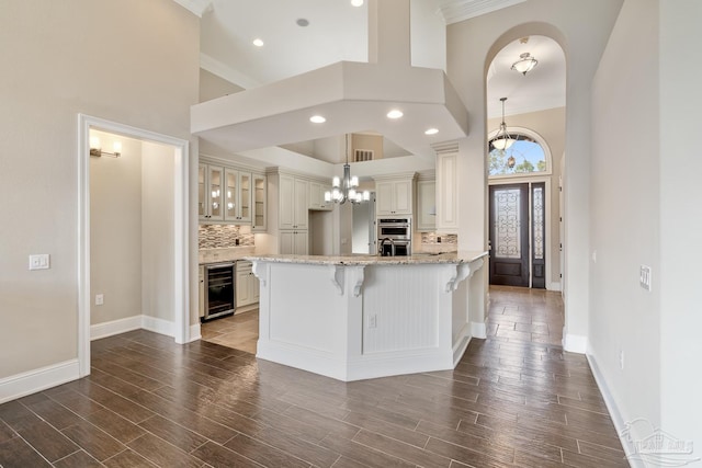 kitchen featuring decorative backsplash, decorative light fixtures, beverage cooler, light stone counters, and a breakfast bar