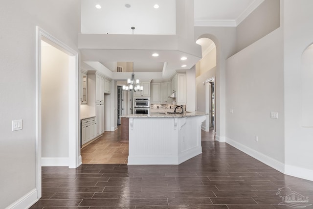 kitchen with a kitchen breakfast bar, hanging light fixtures, a chandelier, double oven, and light stone counters