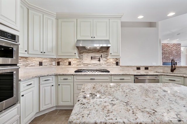 kitchen featuring backsplash, exhaust hood, sink, light stone countertops, and stainless steel appliances