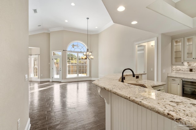 kitchen with wine cooler, a kitchen bar, hanging light fixtures, light stone countertops, and ornamental molding