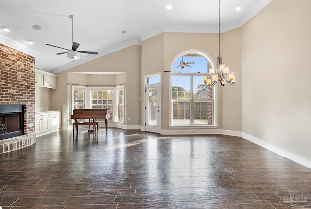 unfurnished living room featuring a brick fireplace, ornamental molding, a towering ceiling, and ceiling fan with notable chandelier