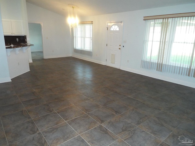 unfurnished living room with a chandelier, baseboards, and lofted ceiling