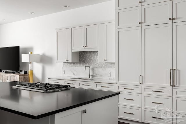 kitchen with tasteful backsplash, white cabinetry, sink, and stainless steel gas cooktop