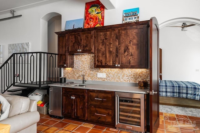 bar with dark brown cabinetry, beverage cooler, sink, and decorative backsplash