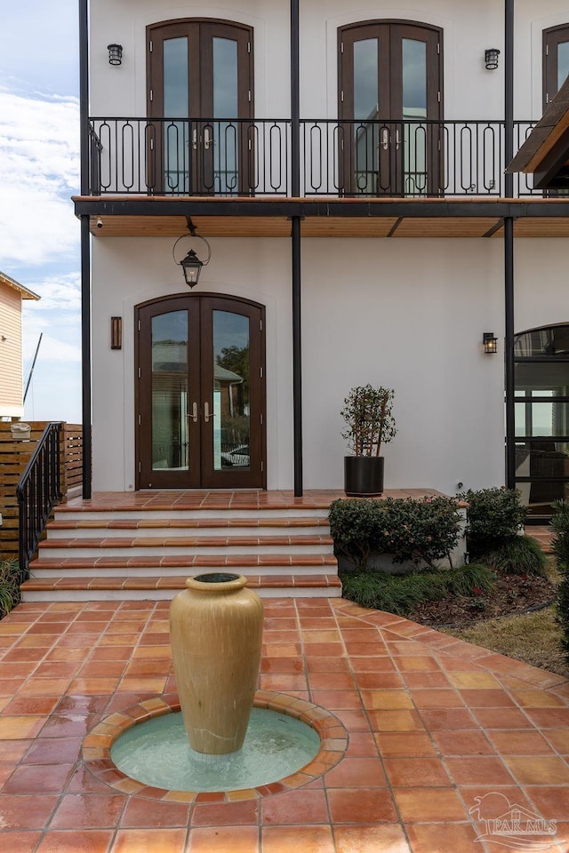 view of exterior entry with a patio area, french doors, and a balcony