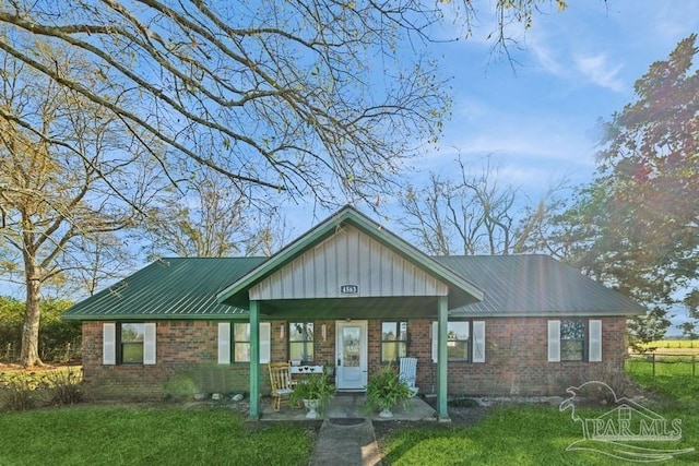 view of front of house with covered porch, a front lawn, metal roof, and brick siding