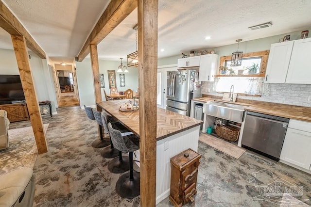 kitchen with tasteful backsplash, butcher block countertops, appliances with stainless steel finishes, decorative light fixtures, and white cabinetry