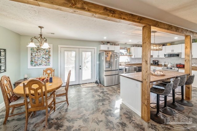 kitchen with tasteful backsplash, hanging light fixtures, appliances with stainless steel finishes, white cabinets, and french doors