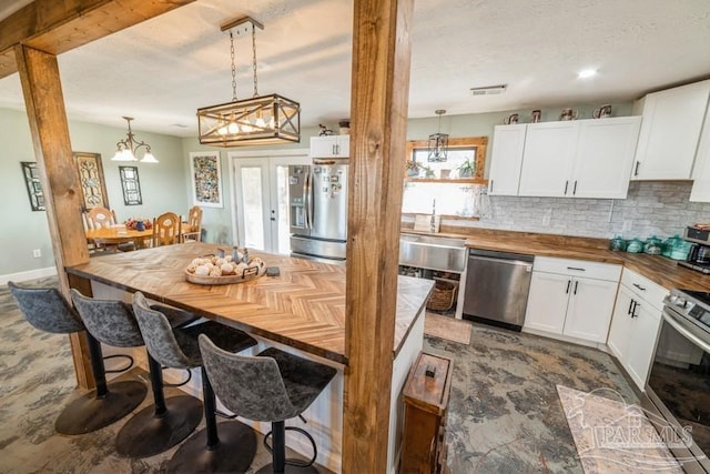 kitchen featuring hanging light fixtures, white cabinetry, butcher block countertops, and appliances with stainless steel finishes