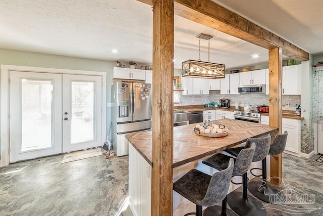 kitchen with stainless steel appliances, wooden counters, hanging light fixtures, white cabinetry, and a kitchen bar