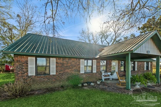 back of property with brick siding, metal roof, and a patio