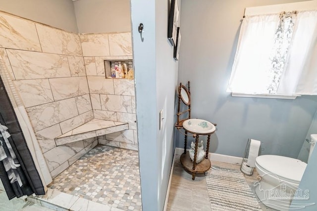 full bath featuring baseboards, a tile shower, and toilet