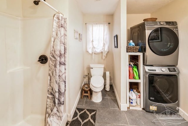 full bath featuring baseboards, stacked washer / dryer, toilet, tile patterned flooring, and a shower stall