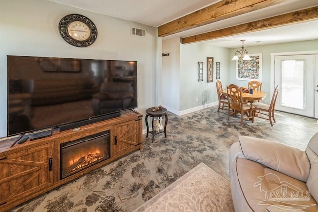 living room featuring beam ceiling, a notable chandelier, visible vents, a glass covered fireplace, and baseboards