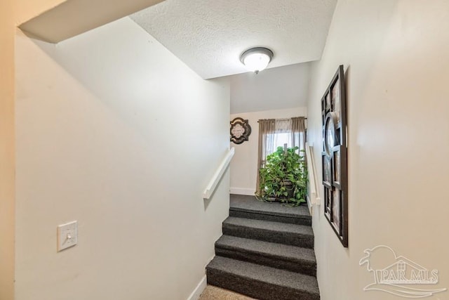 staircase with a textured ceiling, carpet flooring, and baseboards