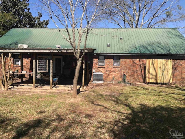 rear view of property with metal roof, brick siding, a lawn, and central air condition unit