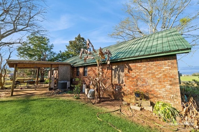 rear view of property with central air condition unit, metal roof, a lawn, and brick siding