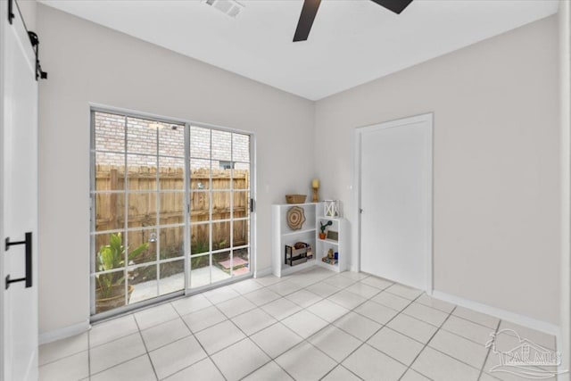 unfurnished room featuring ceiling fan, a barn door, light tile patterned floors, and baseboards